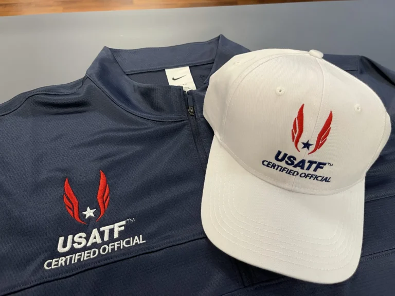 Navy shirt and white cap with matching USATF Certified Official logos