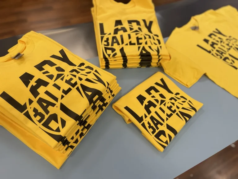 Stacks of yellow Lady Ballers shirts with matching black designs